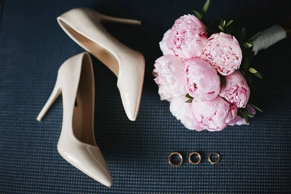 Komposition aus dem Brautstrauß aus schönen rosa Pfingstrosen Blumen mit einem Paar modische Brautschuhe und Eheringe. Konzept der Hochzeitsvorbereitung. Accessoires für eine Braut — Stockfoto