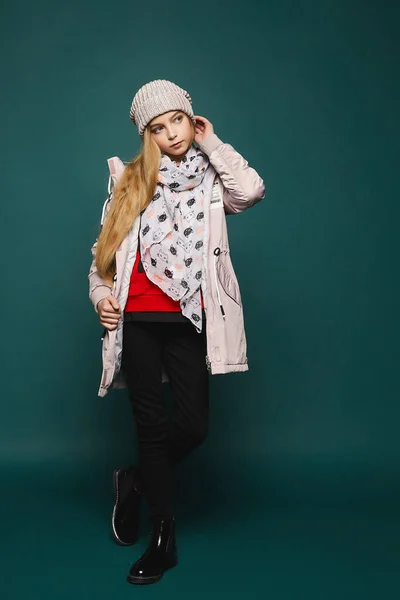 Teenage blondýny modelka v mírném zimním oblečení pózovat přes tmavé pozadí v celé délce. Šťastná dívka v džínách, botách, teplém saku a klobouku. Izolováno na tmavém pozadí. — Stock fotografie