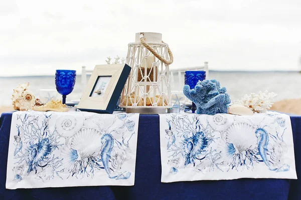 Wedding decoration in a marine style - table for the bride and groom on a sandy beach decorated with sea shells, corals, candlelight and wineglass