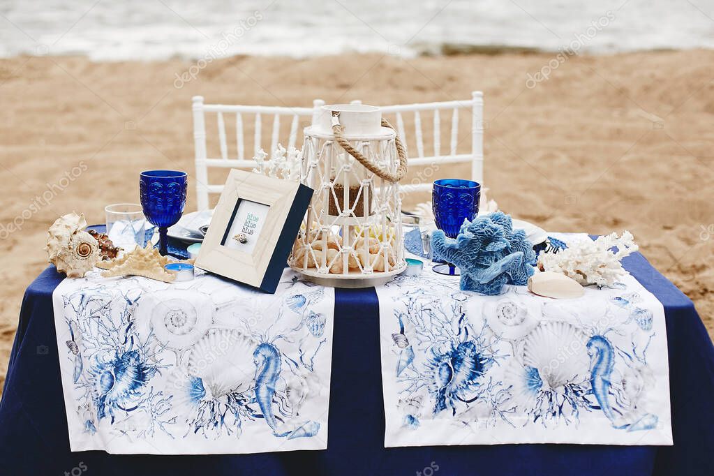 Wedding decoration in a marine style - table for the bride and groom on a sandy beach decorated with sea shells, corals, candlelight and wineglass