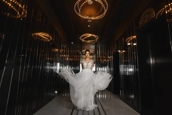 Schöne langbeinige Model-Mädchen in einem Hochzeitskleid zu Fuß durch die dunkle Halle in einem luxuriösen Restaurant. junge Braut im modischen Kleid. Konzept der Hochzeitsmode. — Stockfoto