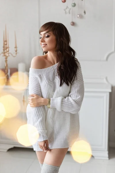 Mooi brunette model meisje in een witte trui poseert tegen de achtergrond van de kerstversiering. De ochtend voor Kerstmis. Vrolijk kerstfeest en fijne feestdagen — Stockfoto