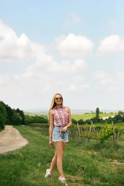 Menina modelo loira com corpo magro perfeito em calções jeans e camisa sem mangas andando no campo. Viagem de verão — Fotografia de Stock