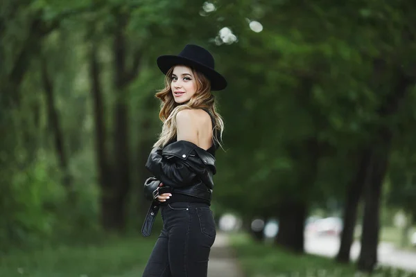 Portrait d'une fille modèle en veste de cuir et chapeau noir posant seul sur une rue de la ville d'été — Photo