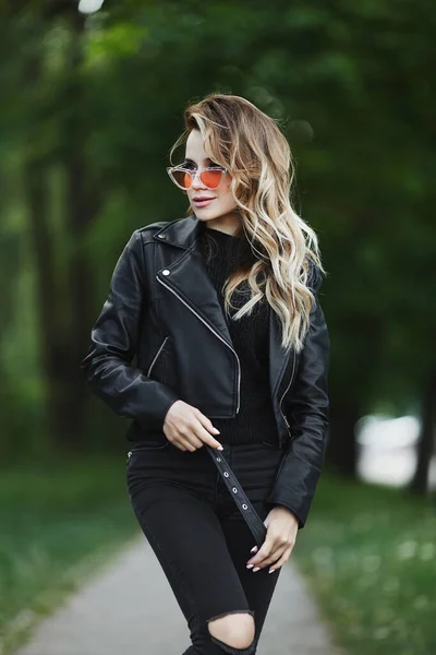 Молода жінка в шкіряній куртці і модні сонцезахисні окуляри ходить на вулиці в літній день — стокове фото