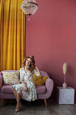 Kokteyl elbisesi ve şapkası olan model kız kameraya bakıyor ve oturma odasında poz veriyor. Yaz modası kavramı