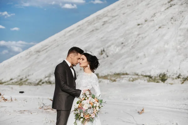 Eine junge hübsche Bräutigam und stilvolle Braut umarmen sich im Freien mit einer schönen Landschaft im Hintergrund — Stockfoto