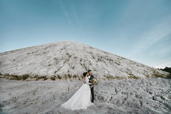 Ein hübscher Bräutigam und eine junge Braut posieren vor der Trauung im Freien mit den Bergen im Hintergrund. — Stockfoto