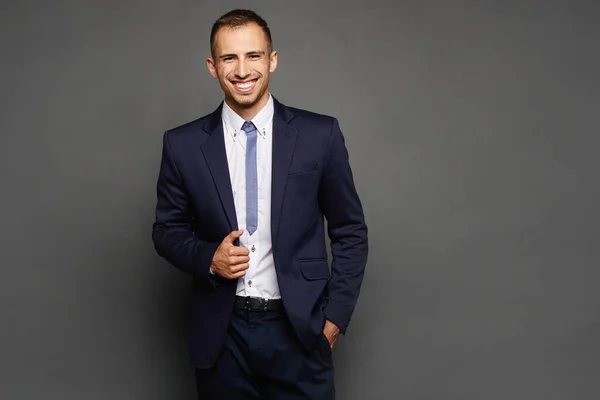 Feliz hombre de negocios en traje aislado en el fondo oscuro. Un joven guapo con un traje oficial posando en el fondo gris . — Foto de Stock