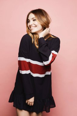 Yaz sporu elbisesi içinde neşeli bir kadın model. Gülümsüyor ve pembe arka planda poz veriyor..