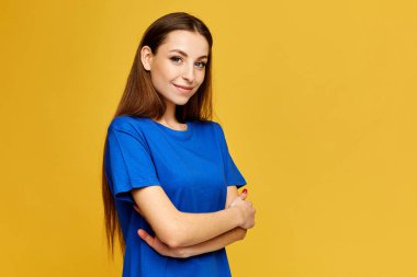 Mavi tişörtlü, sarı arkaplanda poz veren, sağ tarafta fotokopi alanı olan zayıf model kız.