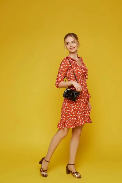 Retrato completo de uma jovem viajante em um vestido e com uma câmera fotográfica no fundo amarelo. Conceito de férias — Fotografia de Stock