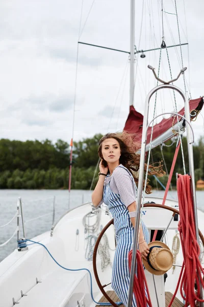 Eine junge Frau in blau gestreiften Overalls posiert an einem windigen Sommertag auf dem Deck einer Jacht — Stockfoto