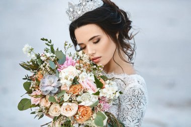 Düğün saç stili ve lüks diyademiyle genç gelin elinde büyük bir buket egzotik çiçek tutuyor.