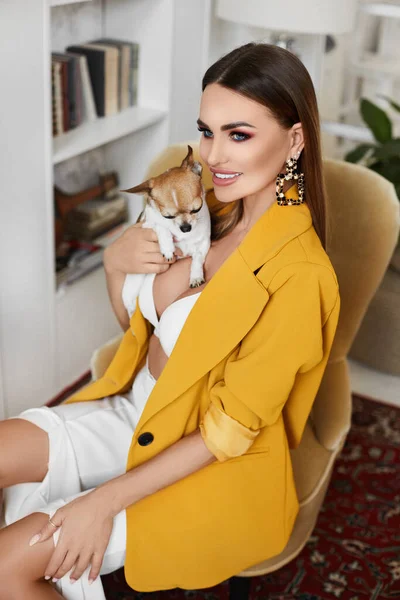 Sexy Model Mädchen mit perfektem Körper in einem gelben Blazer und weißen BH posiert mit niedlichen kleinen Chihuahua-Hund im Inneren — Stockfoto