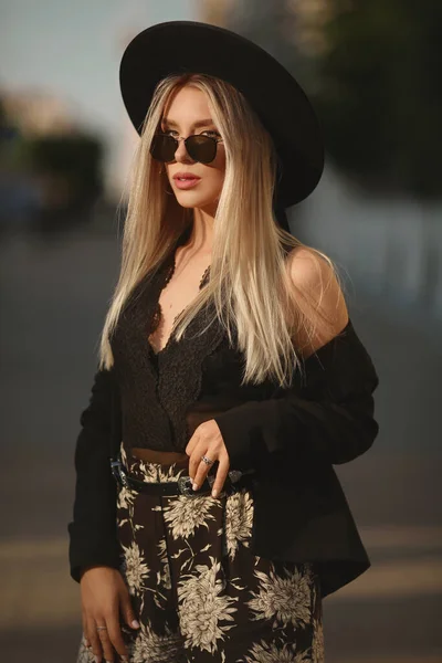 Модель дівчини з світлим волоссям в сонцезахисних окулярах і модний капелюх, що йде один на міській вулиці — стокове фото