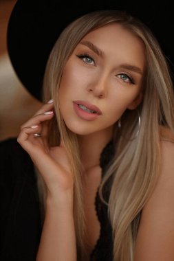 Zarif makyajlı, platin sarısı düz saçlı, siyah modaya uygun şapkalı bir kızın moda portresi.