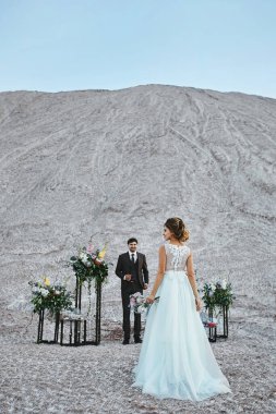 Şık takım elbiseli yakışıklı damat açık hava düğün töreninde gelini bekliyor.