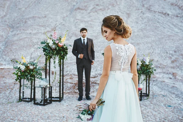 Hezký ženich ve stylovém obleku čeká na nevěstu v luxusních šatech na místě venkovního svatebního obřadu — Stock fotografie