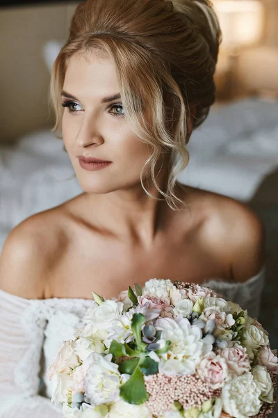 Retrato de uma jovem mulher com coiffure nupcial e em um vestido de casamento com um buquê de noiva em suas mãos — Fotografia de Stock
