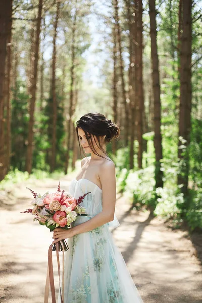 Vista lateral de una adorable joven en un largo vestido de verano con un gran ramo de flores en sus manos al aire libre en el bosque — Foto de Stock