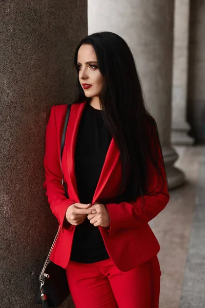 Молодая деловая женщина с красными губами и в красном стильном костюме позирует на улице города — стоковое фото