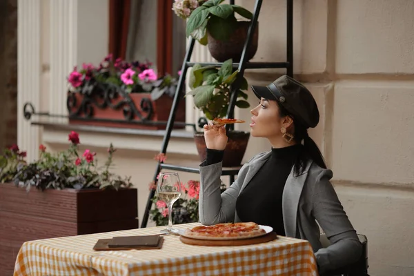 在欧洲的一个城市，一个年轻的女人在户外的咖啡桌上吃披萨 — 图库照片