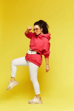 Pembe kapüşonlu ve sarı arka planda duran kemer çantalı genç kız.