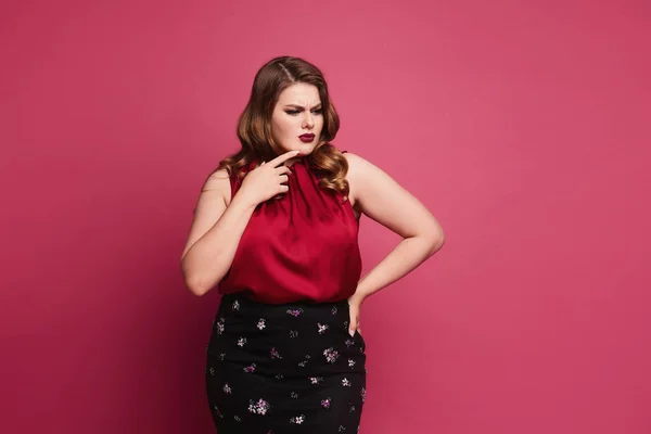 A young plump woman with bright makeup in a red blouse and skirt isolated at the pink background