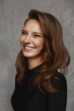 Parlak makyajlı ve siyah elbiseli mükemmel ciltli gülümseyen bir kadının portresi.