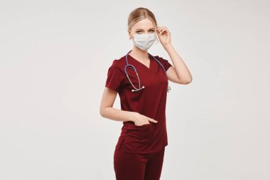 Tıbbi üniformalı ve koruyucu yüzlü genç bir hemşire, beyaz arka planda izole edilmiş. Sağlık ve virüs koruma kavramı.