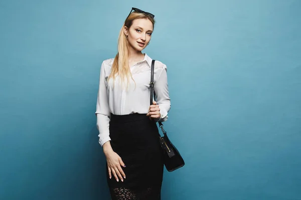 Una joven empresaria en blusa blanca y falda negra mirando a cámara y posando en el fondo azul, aislada —  Fotos de Stock