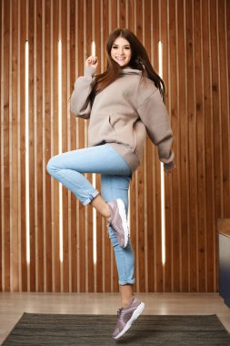 Pembe kapüşonlu, kot pantolonlu, spor ayakkabılı ve iç mekanda poz veren genç bir kız. Spor kıyafetleri giymiş genç bir kadın.