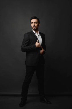 Siyah takım elbiseli, esmer, sakallı yakışıklı bir beyefendinin uzun bir portresi..