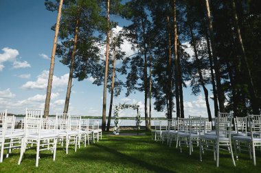 Göl kıyısında düzenlenen açık hava düğün töreni. Taze çiçekler ve boş beyaz sandalyelerle süslenmiş düğün kemeri.