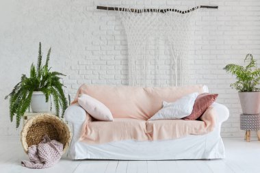 Beyaz kanepenin içi rahat. Beyaz tuğla duvarın arka planında iki kova bitki ve ahşap zemin boyalı.