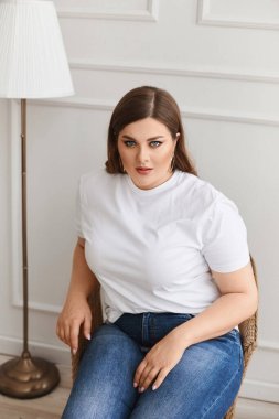 Ayrıca kot pantolonlu ve beyaz tişörtlü manken kız oturma odasındaki koltukta oturuyor. XXL modası.