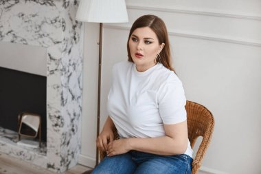 Ayrıca kot pantolonlu ve beyaz tişörtlü manken kız oturma odasındaki koltukta oturuyor. XXL modası.