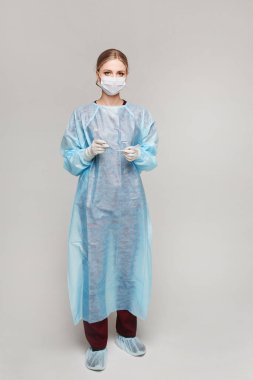 Koruyucu kılıflı ve maskeli genç bir kadın doktor mavi arka planda endotrakeal tüp tutuyor, izole edilmiş. Sağlık ve Acil Durum Konsepti
