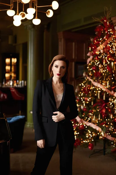 Siyah takım elbiseli bir iş kadını Noel partisi için dekore edilmiş lüks bir iç mekânda poz veriyor. — Stok fotoğraf