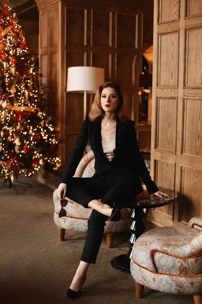 Jovem senhora de negócios em terno elegante preto posando no interior de luxo decorado para festa de ano novo — Fotografia de Stock