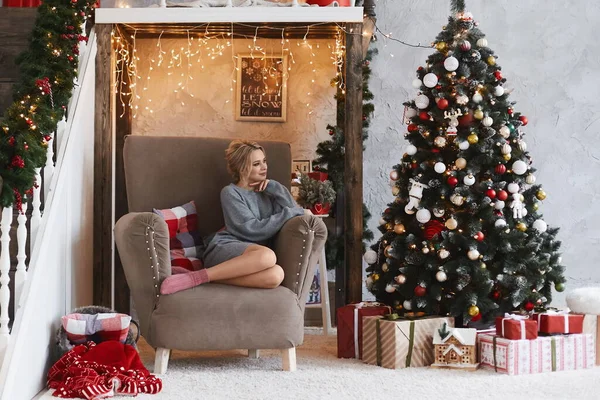 Modell lány egy pulóver és csupasz lábak ül karosszékben közel karácsonyfa karácsony reggel — Stock Fotó