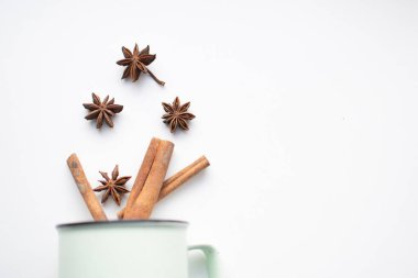 Yıldız anason ve tarçın beyaz arka planda bir kupadan dökülür. Bu aromatik baharatlar sıcak şarap yapımında kullanılır. Metin için boşluk