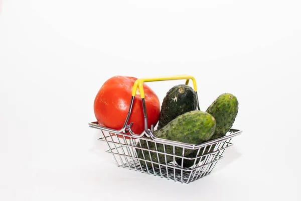 a small grocery basket contains fresh vegetables (tomatoes and cucumbers) on a white background.