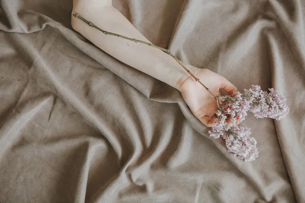 一个女孩的手与丁香树枝在床上皱巴巴的床单 — 图库照片
