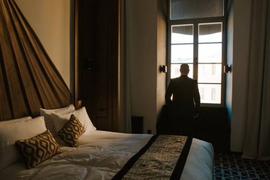 büyük bir pencere yakınında şık bir yatak odasında elbiseli adam