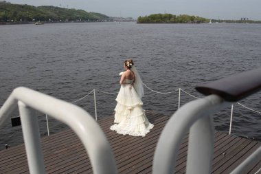 beyaz bir elbise içinde gelin nehir ve şehrin köprüleri ile bakan bir iskelede duruyor