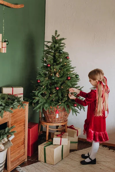 Bordo elbiseli kız rustik bir odada bir Noel ağacı süsle