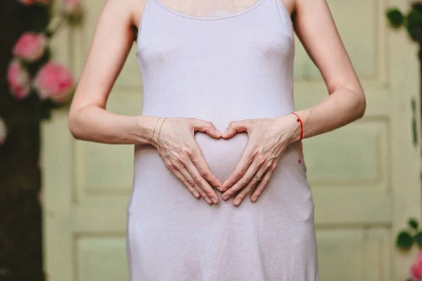 妊娠中の女の子が彼女の胃の彼女の心で彼女の手を保持しています — ストック写真