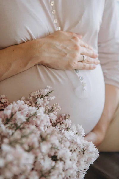 妊娠中の女性は 新鮮な花の背景に手で彼女の腹を保持しています — ストック写真